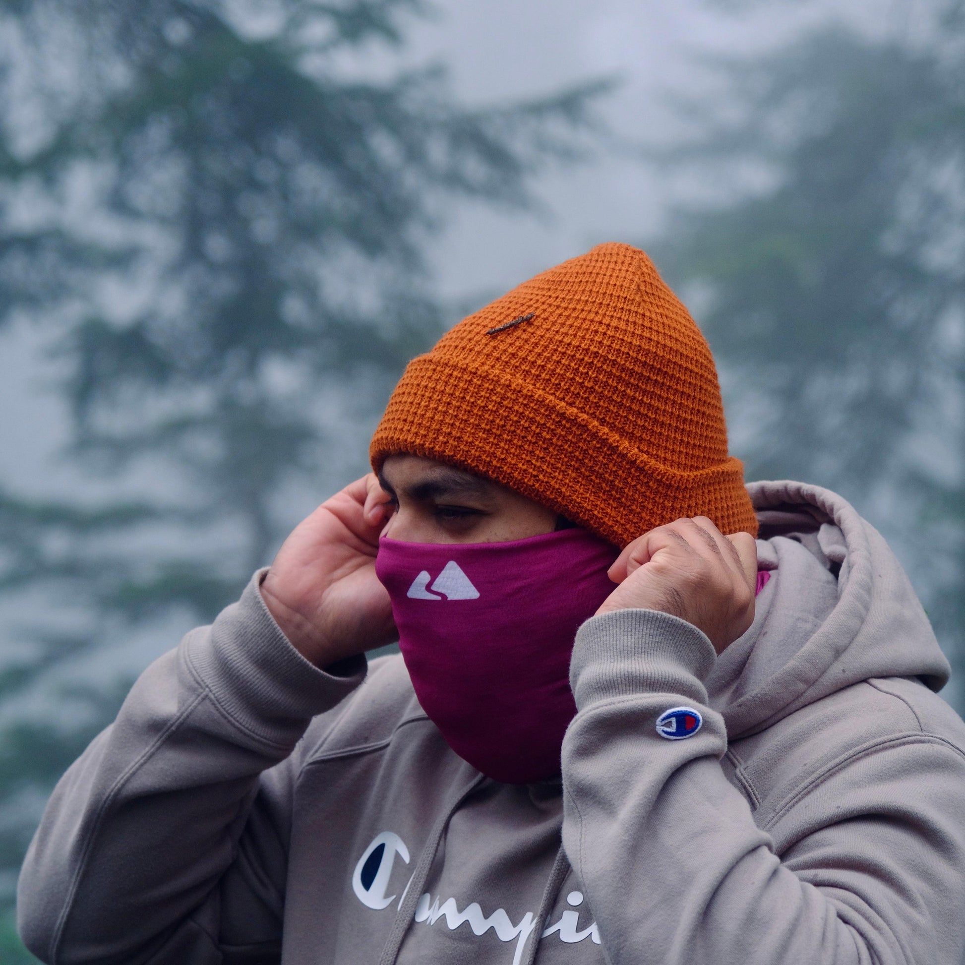 Neck buff gaiter displayed on a male model. With a white mountain logo. Burgundy