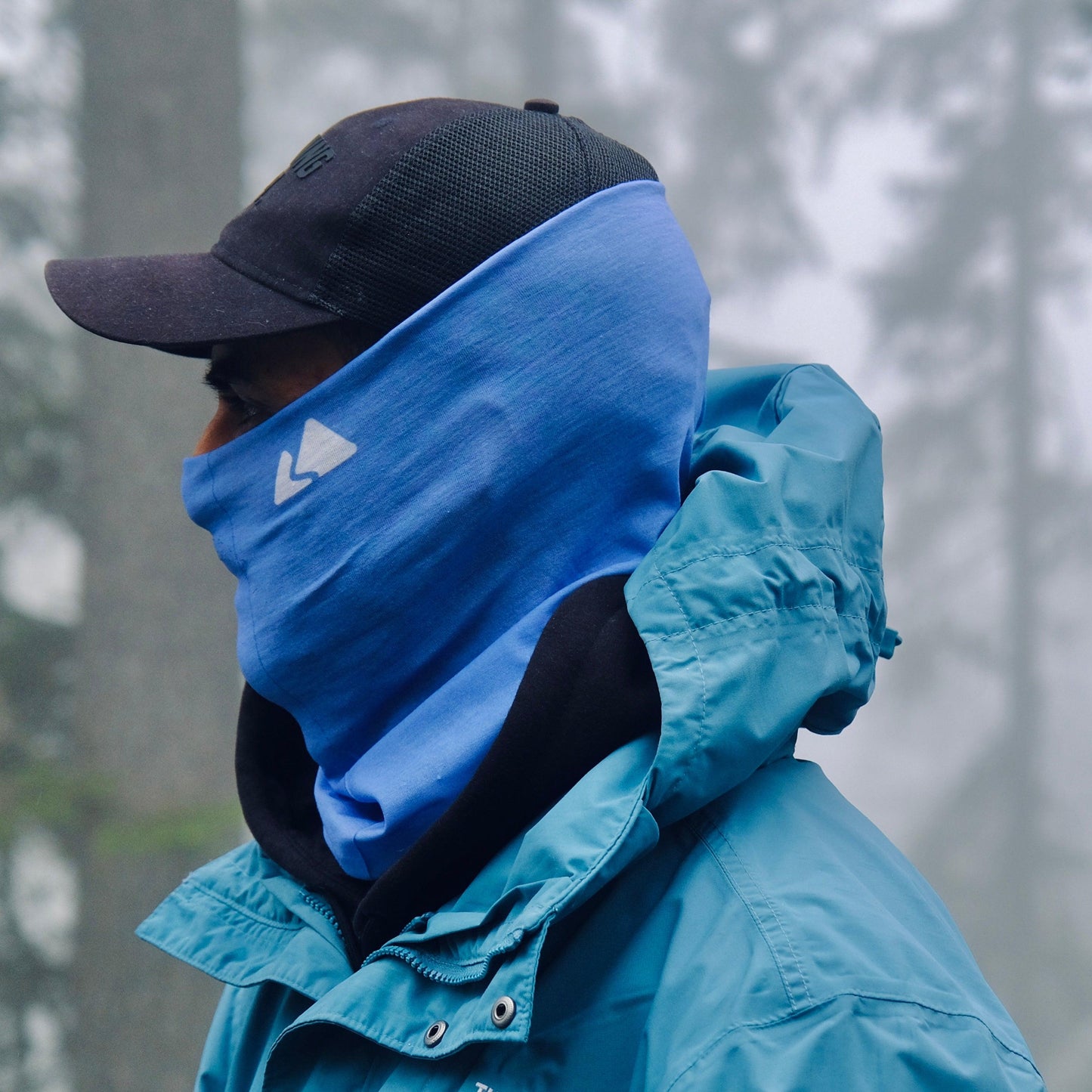 Neck buff gaiter displayed on a male model. With a white mountain logo. Day Sky Blue colour. 